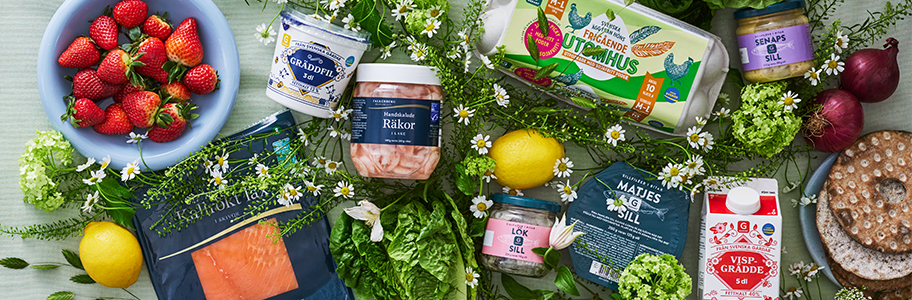 Ett bord med midsommarvaror som ägg, jordgubbar, citron, räkor, grädde, sill, lax, gräddfil och knäckebröd.