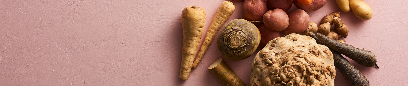 Palsternacka, Potatis Asterix, Morot, Potatis Amadine, Jordärtsskocka, Kålrot, Rotselleri, Lila morot och Pepparrot på ett rosa bord.