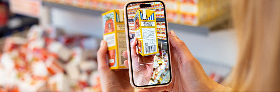 En hand som håller i en mobiltelefon och riktar kameran mot en streckkod på en förpackning krossade tomater för att scanna den.