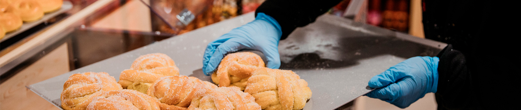En medarbetare med blåa plasthandskar plockar sockerbullar från en metallplåt